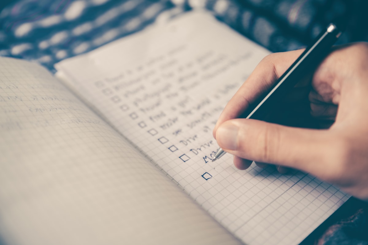A hand writing notes in a paper notebook next to a cup of tea